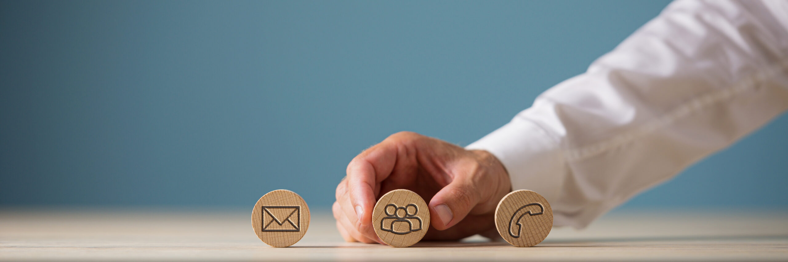 Wide view image of customer service representative placing three wooden cut circles with contact and information icons on them in a row.
