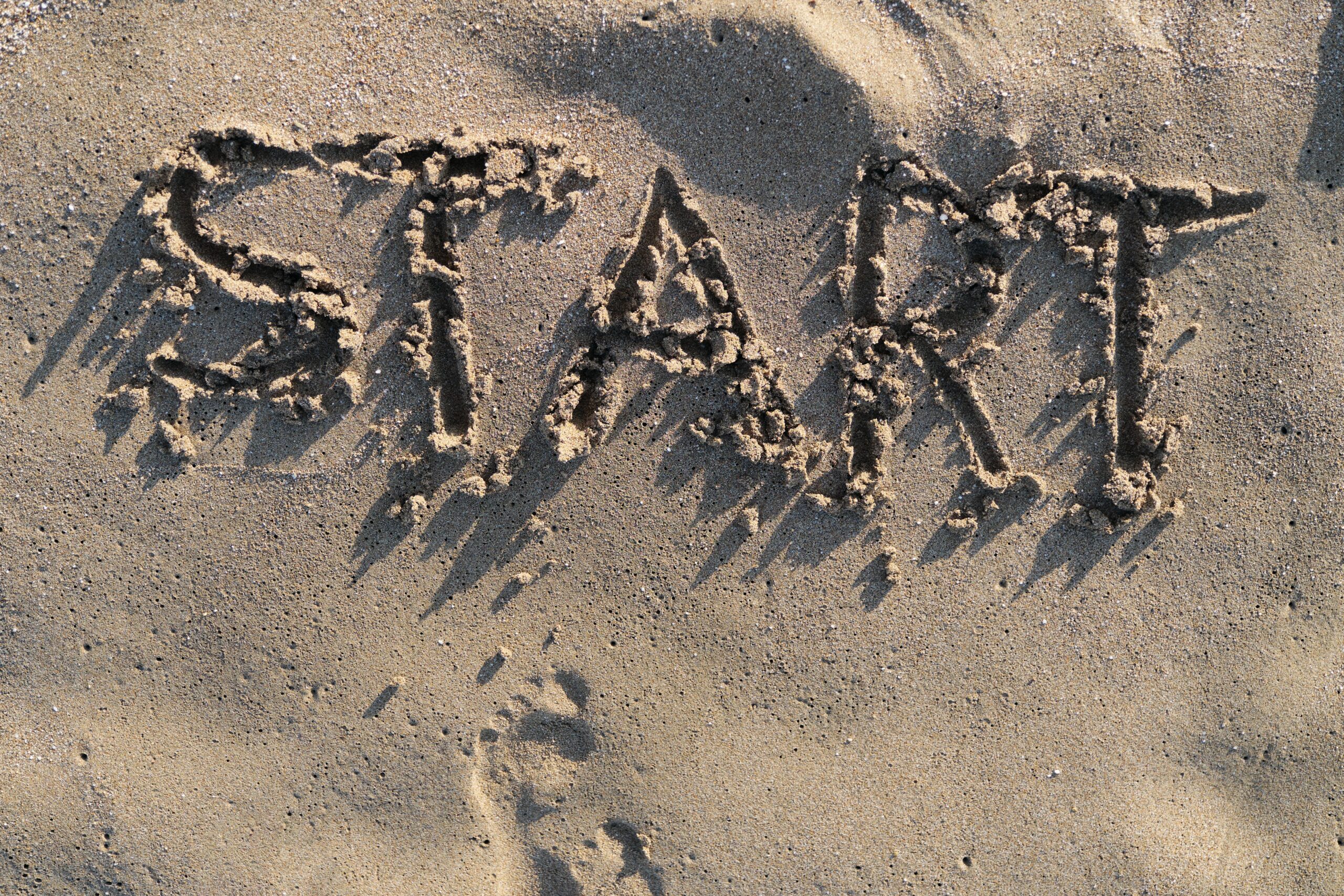 Text start written in sand on sea beach and bare footprints facing the word.
